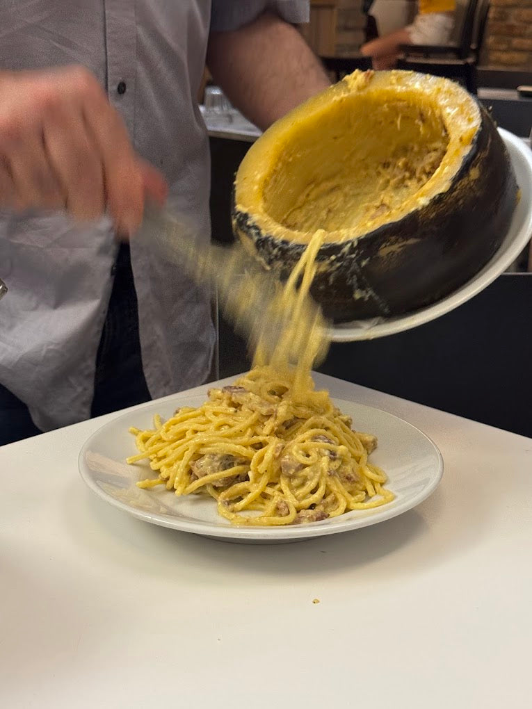 Roman carbonara being served from a Pecorino cheese wheel
